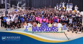 Large group of Athletes at Westcliff University posing for a photo. In the front there is a sign that reads go warrioers.